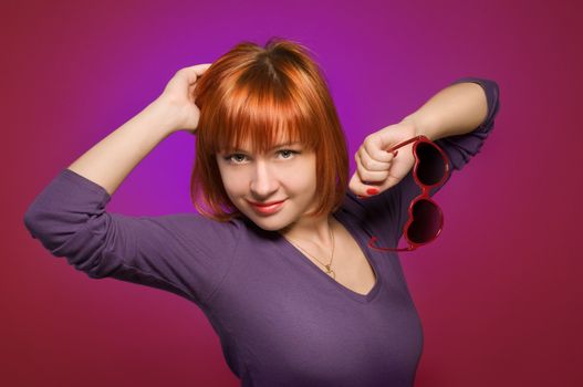 Portrait of beautiful red woman wearing heart-shaped sunglasses posing at the studio