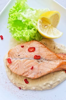 Grilled salmon steak with greens, lemon, sauce and pepper chile