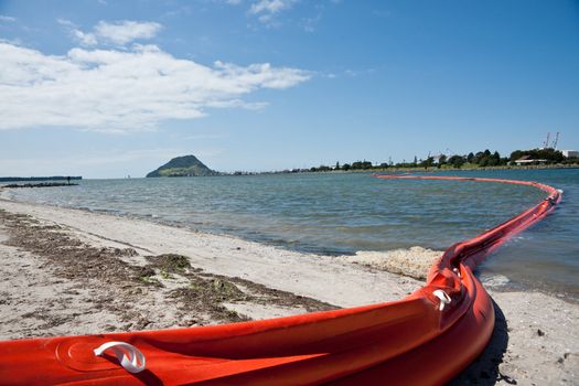 Orange oil boom snakelike across Tauranga harbour protects the beaches from contamination risk.