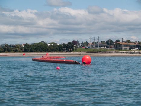 Orange oil boom snakelike across Tauranga harbour protects the beaches from contamination risk.