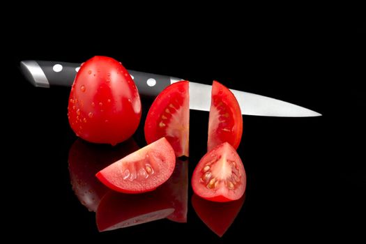 A knife, a whole fresh tomato and a fresh cutted tomato on a black reflecting background with copyspace