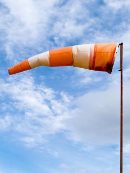 Red and white windsock wind filled partially clouded blue sky background