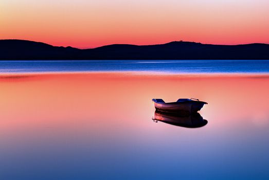 Scenic view of small fishing boat in calm water at sunset with hills in the background.