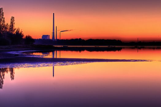 Scenic view of power plant near beach in calm water at sunset