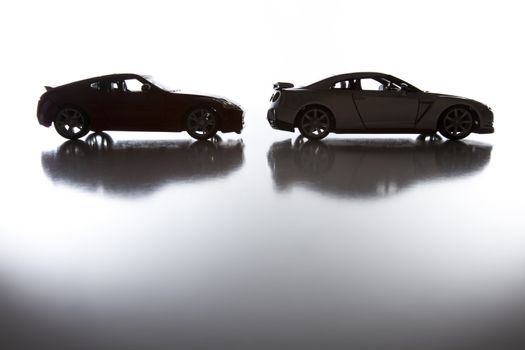 Silhouette of Sports Cars on Reflective Surface Against a White Background.