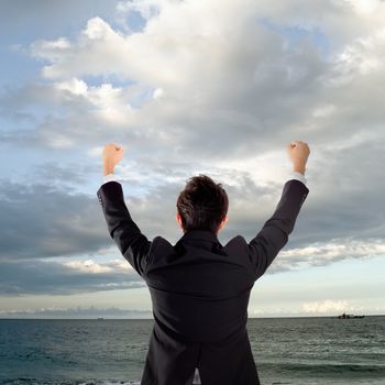 Cheerful business man standing in outside of ocean and rising hands.