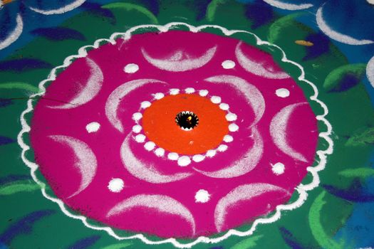 A lamp lit in between a traditional design made of colorful powder called Rangoli, on the occassion of Diwali festival in India.