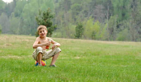 little boy with a colour ball sitting on the gass