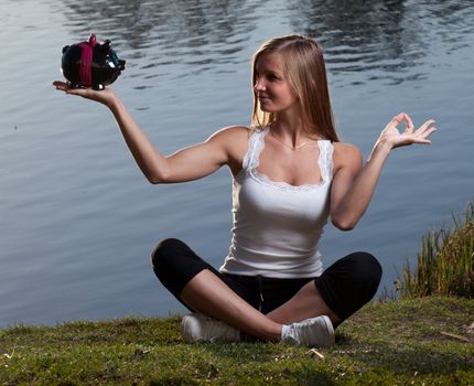 a young woman with a piggy bank meditating in front of a lake