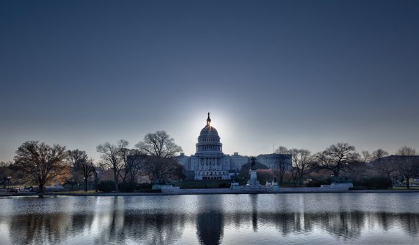 Brightly lit dawn sky behind the illuminated dome of the Capitol in Washington DC with the pool and statues