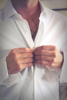 Groom buttons his shirt before the wedding ceremony