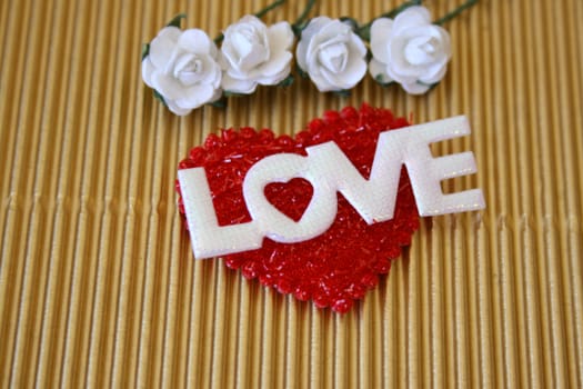 The word love on a soft red heart with white roses