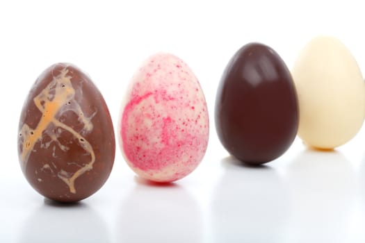 Four unique hand made easter eggs standing in a row.  Flavours are: Chocolate with orange chips, white chocolate and pieces of strawberry crunch, pure dark chocolate and pure white chocolate.  White background.