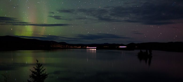 Night Sky Stars, clouds and faint Northern Lights over dark road at lake shore, Yukon, Territory, Canada.