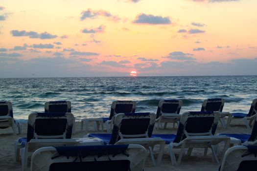 Sunrise over Riviera Maya beach with lounge chairs