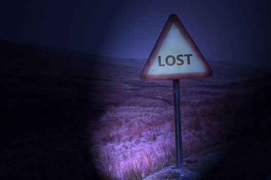 Night shot of a single road warning sign with the word 'lost' illuminated by car headlights with subtle remote and dark landscape behind.