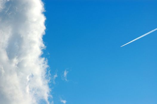 Cloud against a blue sky and airplane smoke trail.