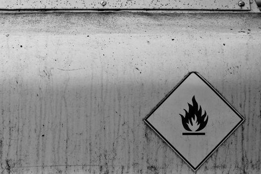 Flammable material weathered warning sign on rusty metal surface. Black and white.