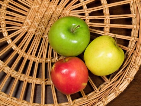 Three colored apples on wicker plate at the table