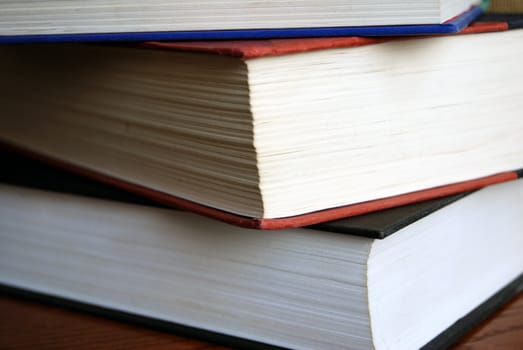 Horizontal image of several books stacked upon each other sitting on a wooden table.