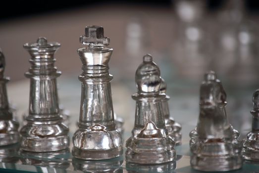 Horizontal image of a glass chess set, with focus on closest pieces and the opposing side falling out of focus in the shallow depth of field.