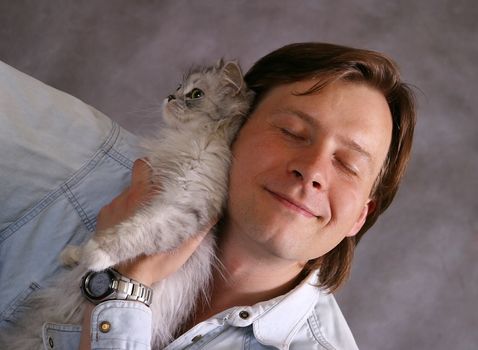 Man covers a kitten on a grey background