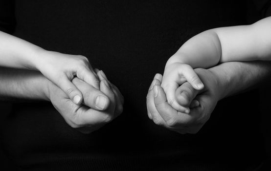 Hands of the father and his daughters on a dark background