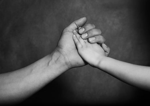 Hand of the adult person and hand of the small child on a dark background