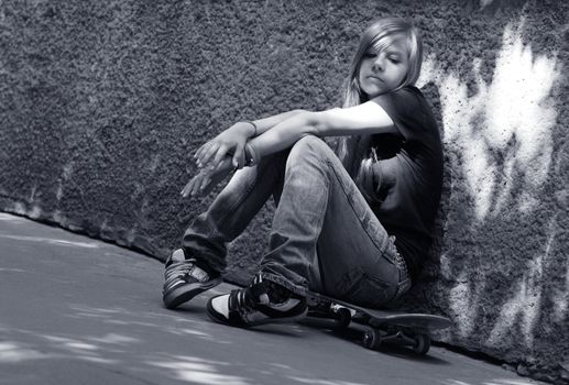 The girl with skateboard sitting against a wall. Shadow on a wall as a wing