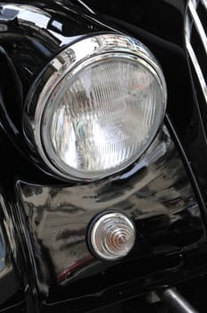 Close-up of an old chromed headlight on a black Morgan car