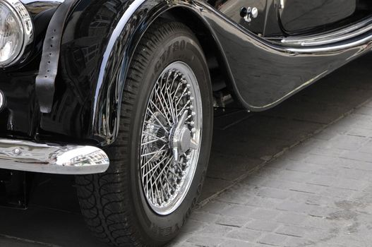 Old chromed head wheel of a black Morgan car