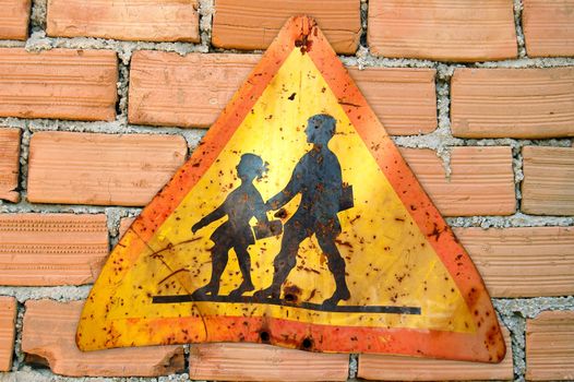 Brick wall and rusty warning sign for school children.