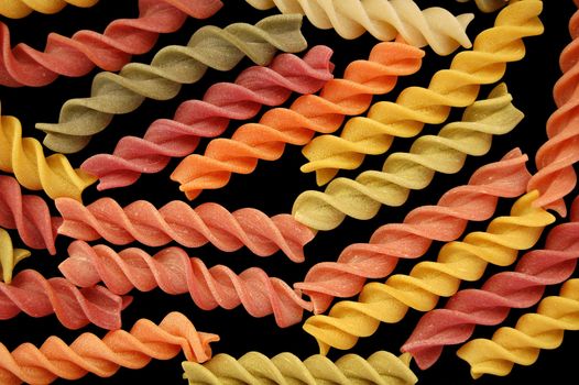 Different flavors of fusilli twists pasta against a black backgrround.