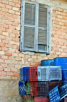 Abandoned house window and brick wall. Rusty metal barrels, plastic crate containers.