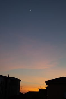 Sunset with moon over silhouettes of houses