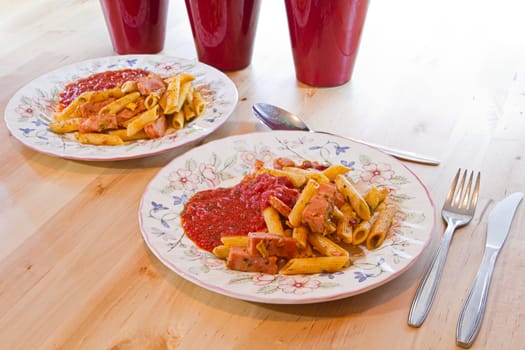 Two plates penne macaroni with spicy ham and tomato-basil sauce on wooden table