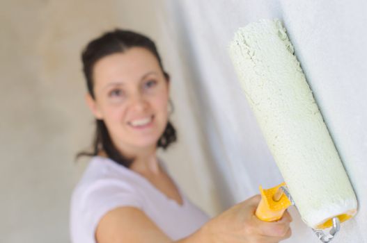 Young Woman painting a wall with roller .