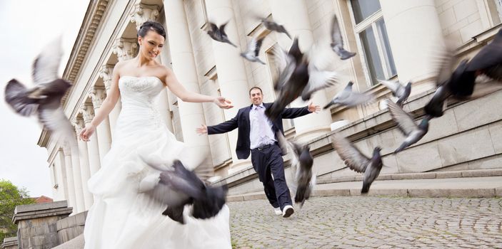 Happy bride and groom walking behind flying grey doves