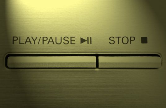 Close up on two buttons on a chrome electronic device with the words 'play/pause' and 'stop' with yellow light effect filter