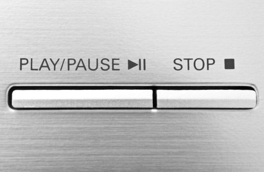 Close up on two buttons on a chrome electronic device with the words 'play/pause' and 'stop'