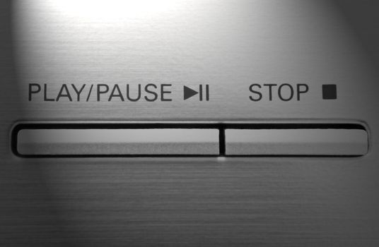 Close up on two buttons on a chrome electronic device with the words 'play/pause' and 'stop' with light effect filter