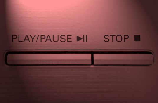 Close up on two buttons on a chrome electronic device with the words 'play/pause' and 'stop' with red light effect filter