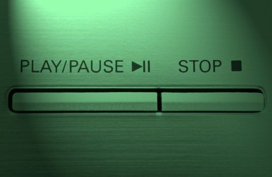 Close up on two buttons on a chrome electronic device with the words 'play/pause' and 'stop' with green light effect filter