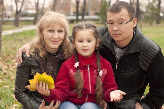 The young family in park, sits on a grass and smiles