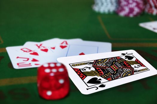 green casino table with dice and a hand of a royal flush in a poker game and the jack of spades in the pack