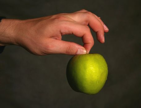 Man's hand with a green apple on a dark background