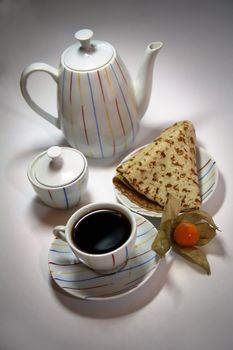 Teapot, cup from coffee and a pancake on a plate, decorated with a yellow berry