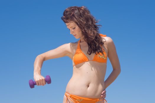 Model in orange bikini posing with a dumbbell