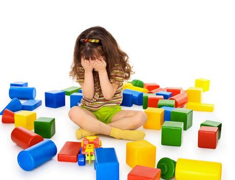 A little girl sitting on a white background among the toys and crying