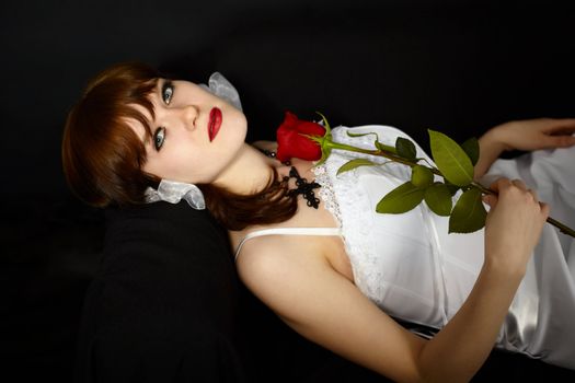 Young beautiful girl with rose in his hand lying on a black background